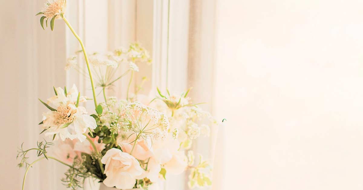 Wildflowers in white vase on windowsill in morning sun.