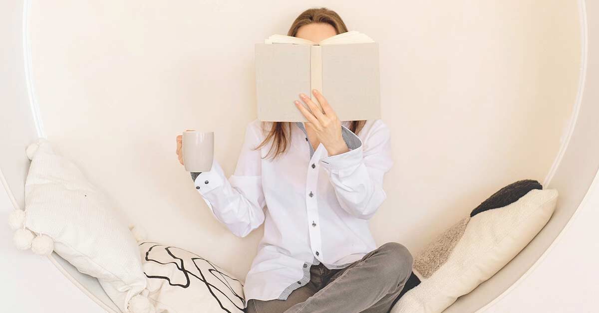 Woman taking it slow by sitting in circular seat while holding coffee mug and reading.