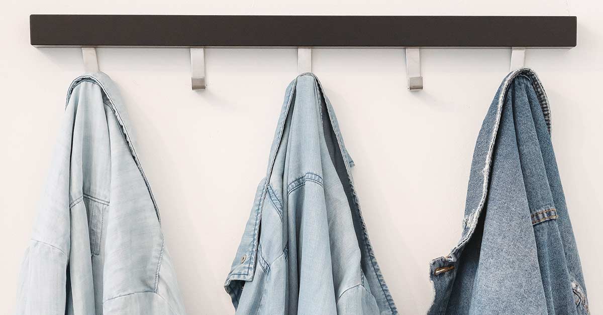 Denim shirts and jackets that need to be decluttered hanging on hooks against white wall.