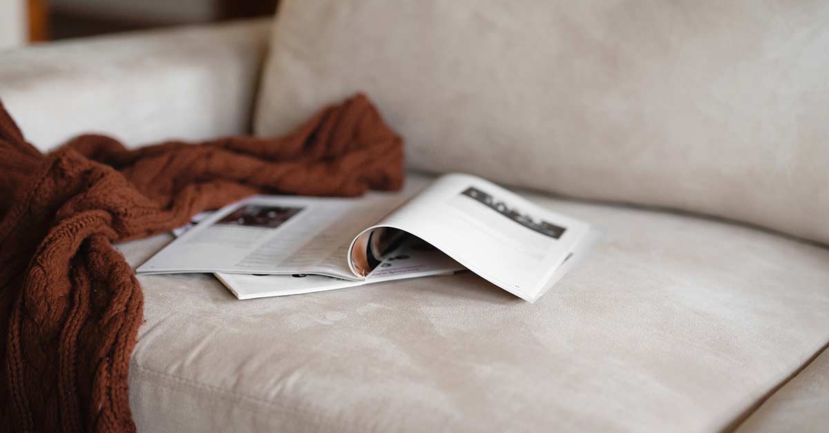 Open magazines and brown knit blanket left on white couch.