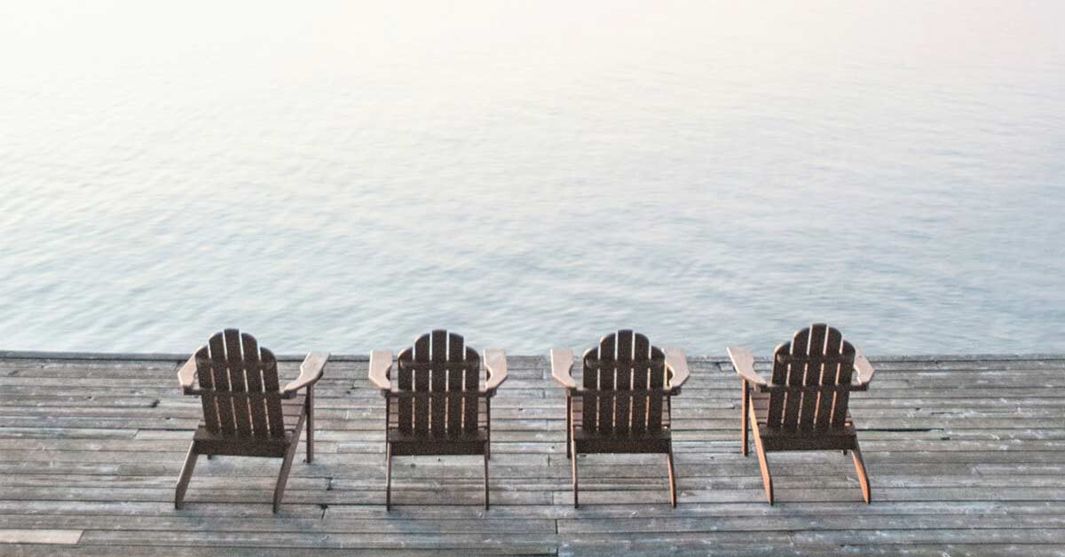 Four empty chairs on lake dock waiting for someone to enjoy a slow day.