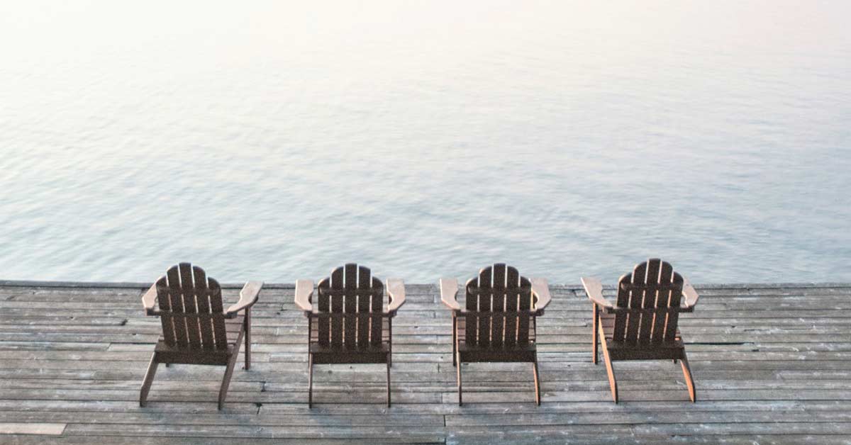 Four empty chairs on lake dock waiting for someone to enjoy a slow day.