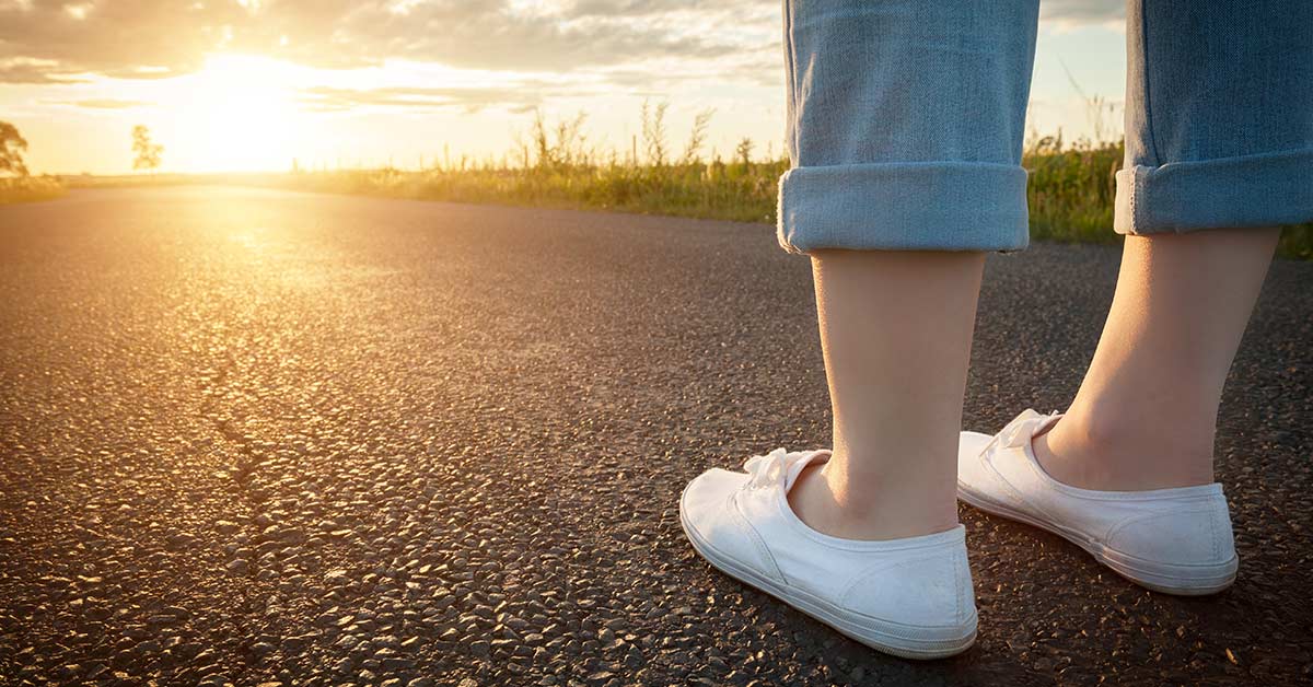 Woman standing on road watching the sunrise as she prepares to start slow on her morning walk.