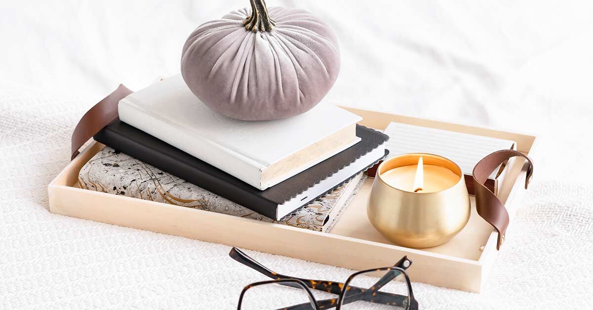 Tray with creative writing journals and candle on white blanket.