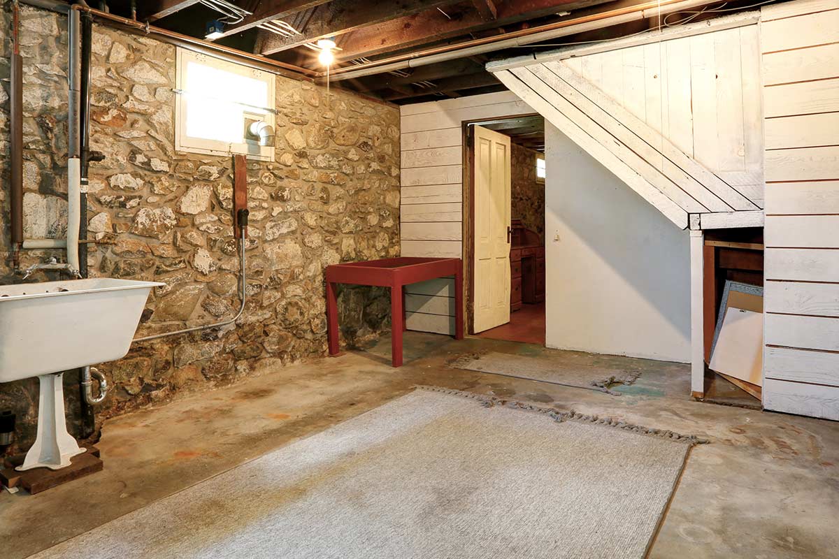 Clutter-free basement with laundry sink, table, and rug.