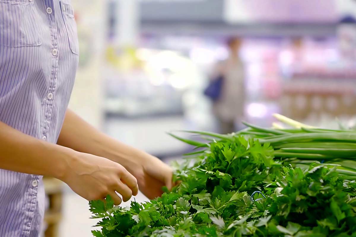 Woman in blue shirt choosing green vegetables during a monthly grocery shopping trip.