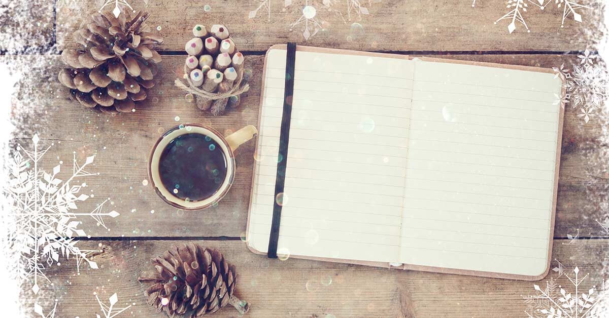 Winter creative writing flatlay with open journal, coffee, pencils and pinecones on wood table with snowflake overlay.