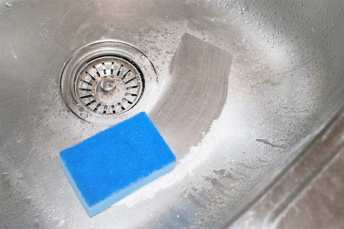 Blue sponge and cleaning powder in stainless steel sink.