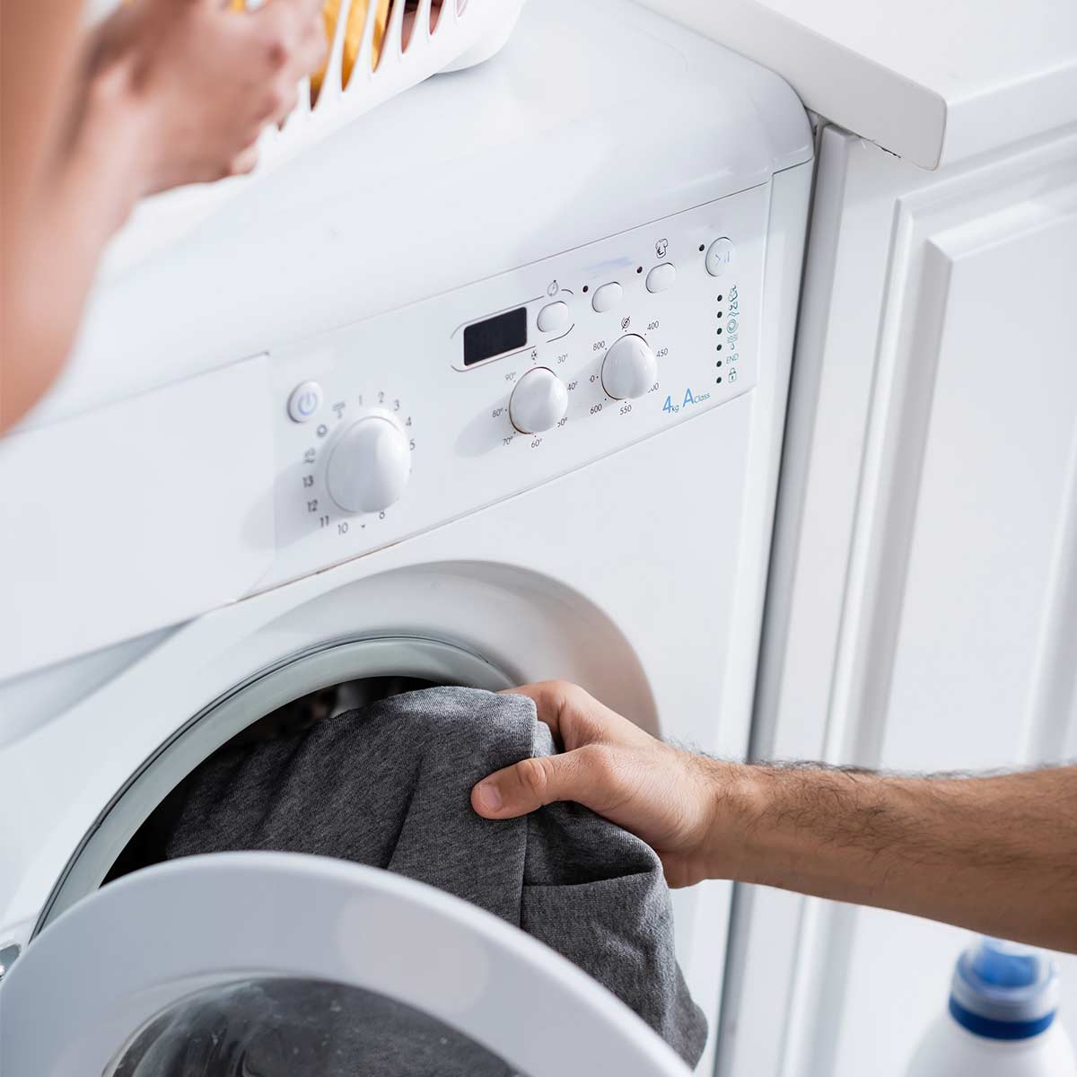 Male hand unloading dryer and female hand touching laundry basket of clean clothes on top of dryer.