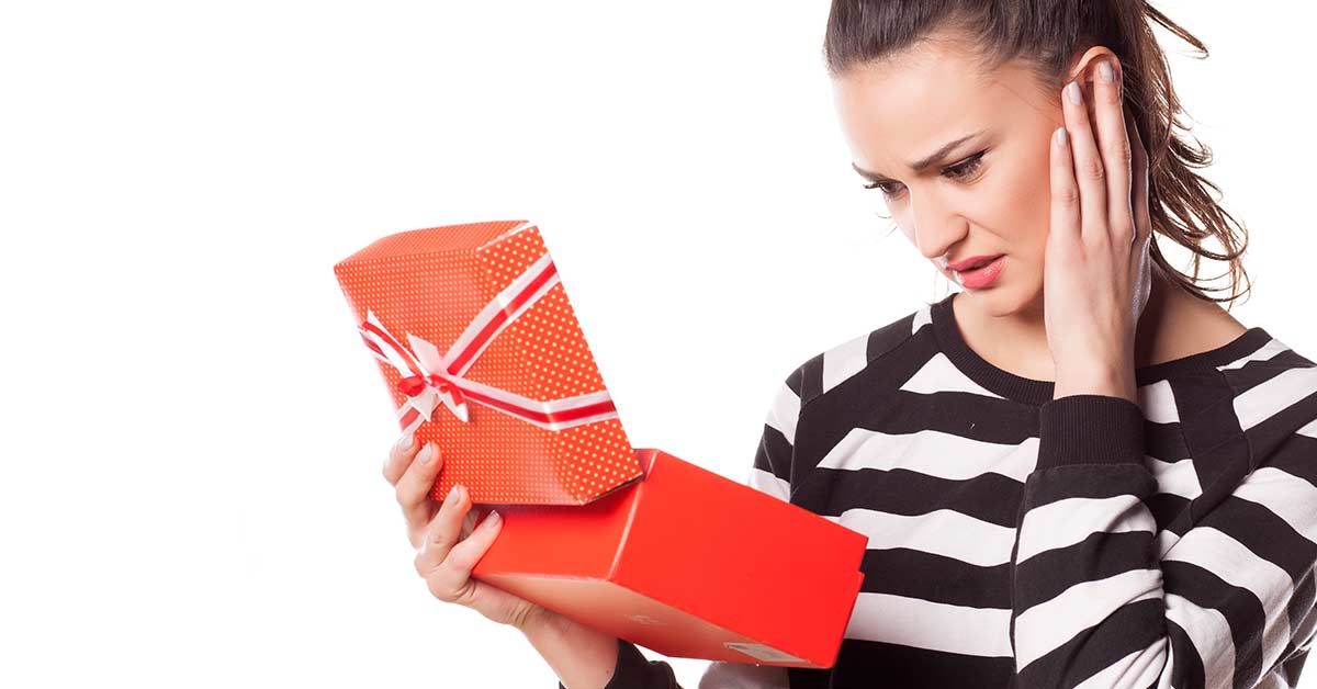 Woman wearing a black and white striped shirt and expressing disbelief at the contents of an open red gift box.