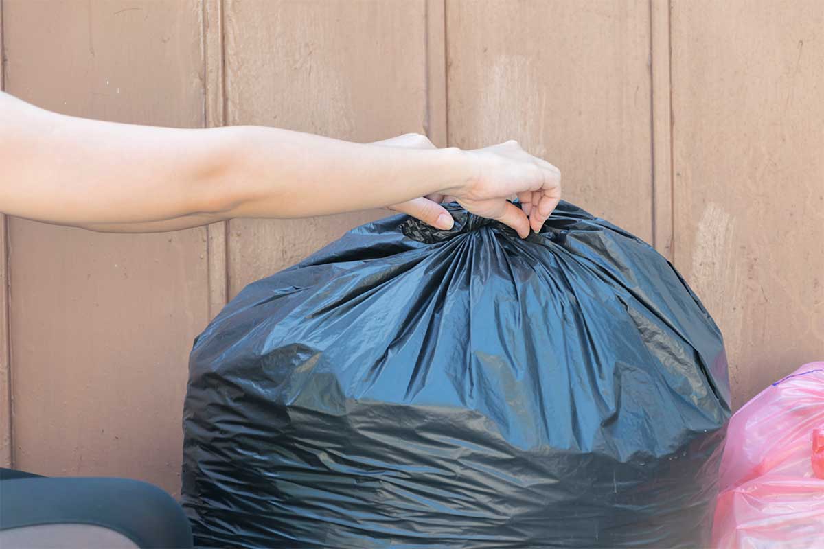 Woman tying a bag of trash after removing it while helping a hoarder clean.