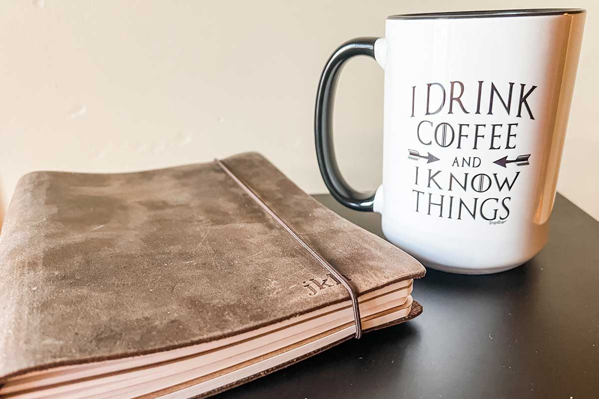 I drink coffee and I know things favorite mug next to leather journal.