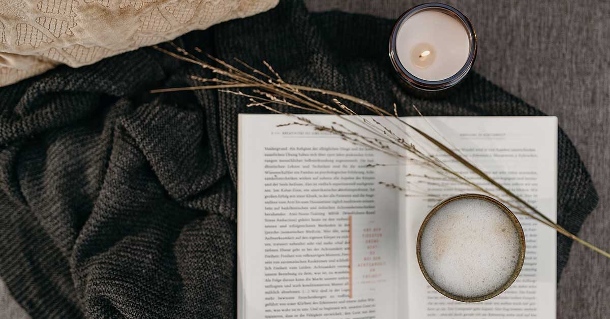 Overhead shot of blankets book candle and drink ready for a perfect morning routine.