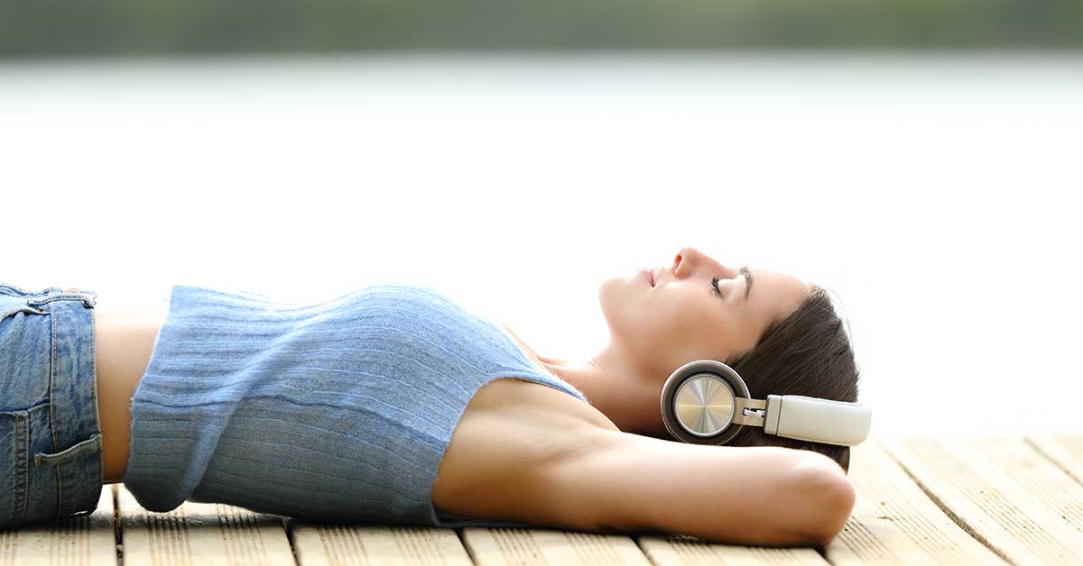 Woman wearing headphones and lying on dock on a summer day.