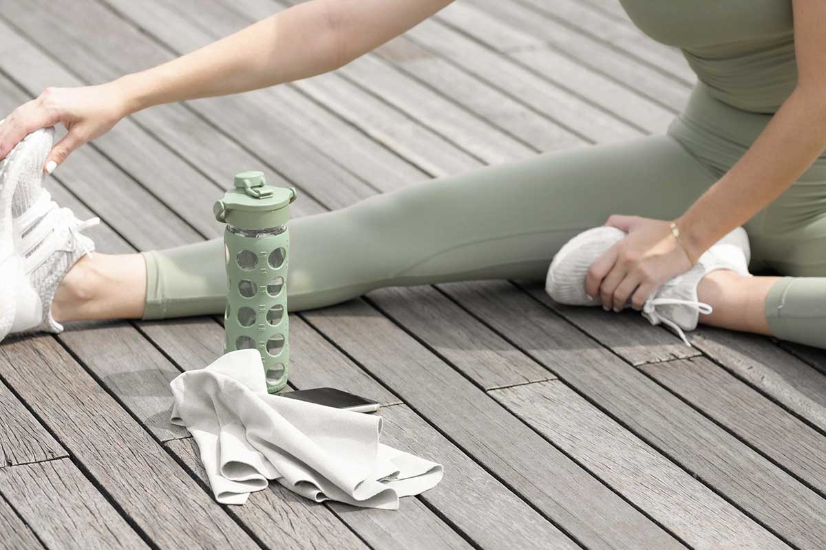 Woman wearing green workout clothes stretching on wood deck next to water bottle and phone.