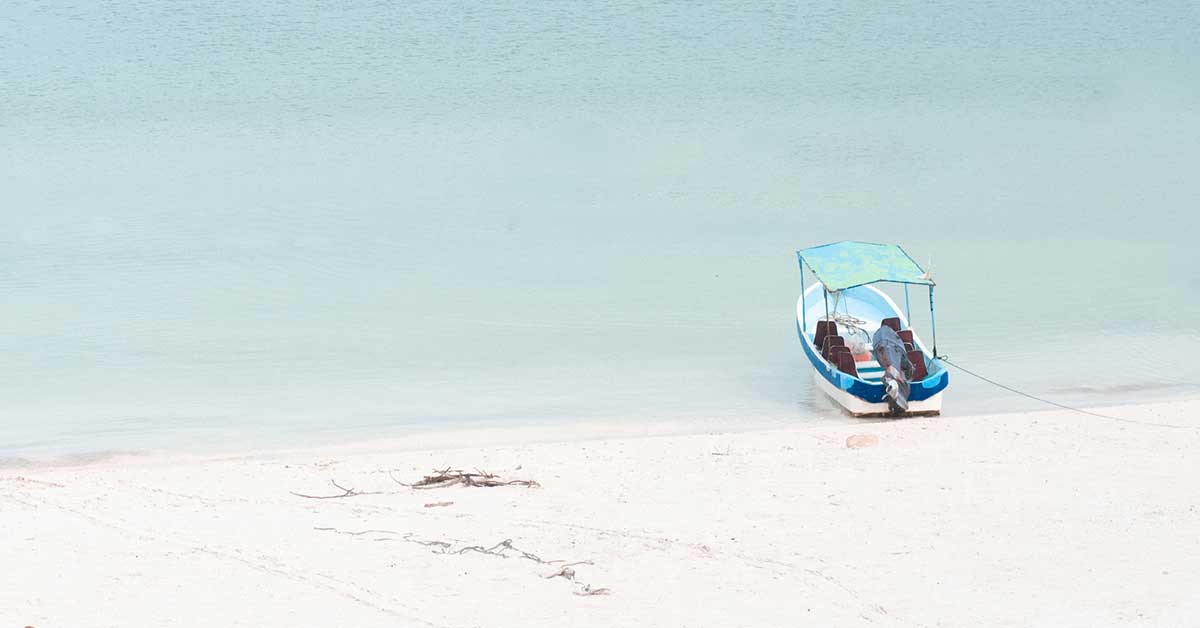 Small blue and white boat anchored at ocean beach on a sunny summer day.