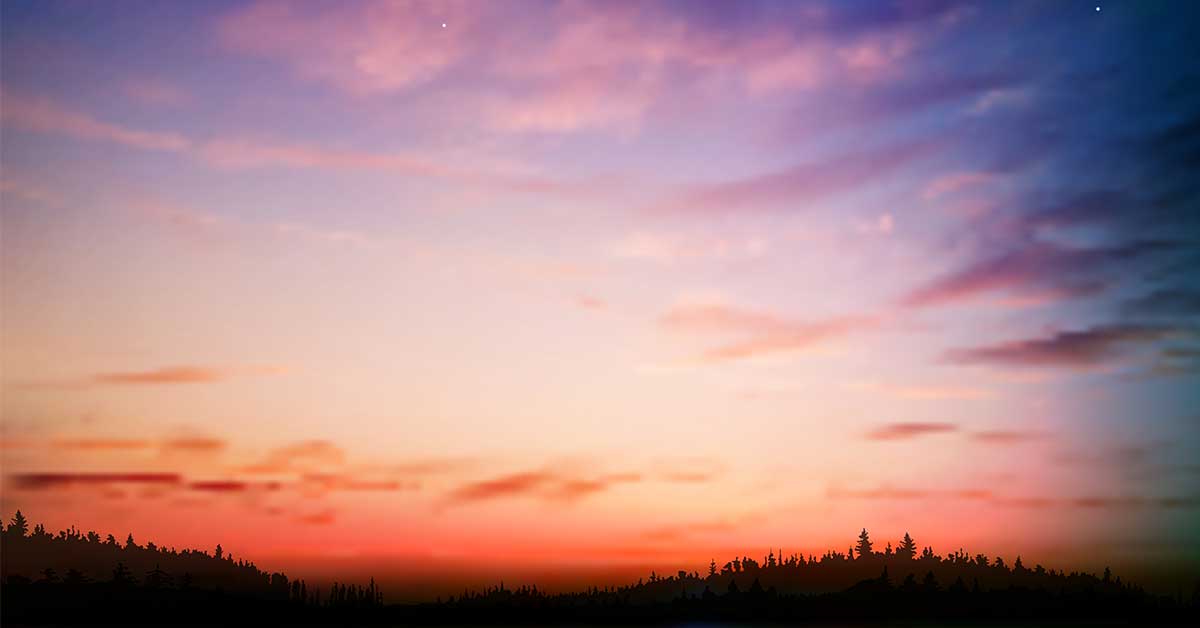 Summer nights aesthetic sunset with orange pink and purple sky over dark wooded hills.