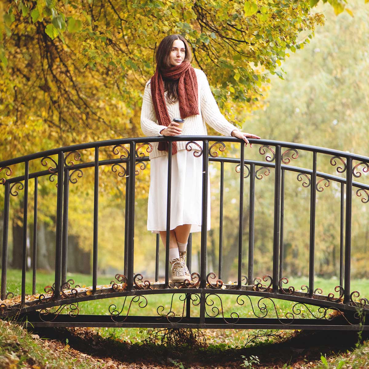 Woman wearing skirt and cozy sweater standing on small metal bridge on an autumn day.