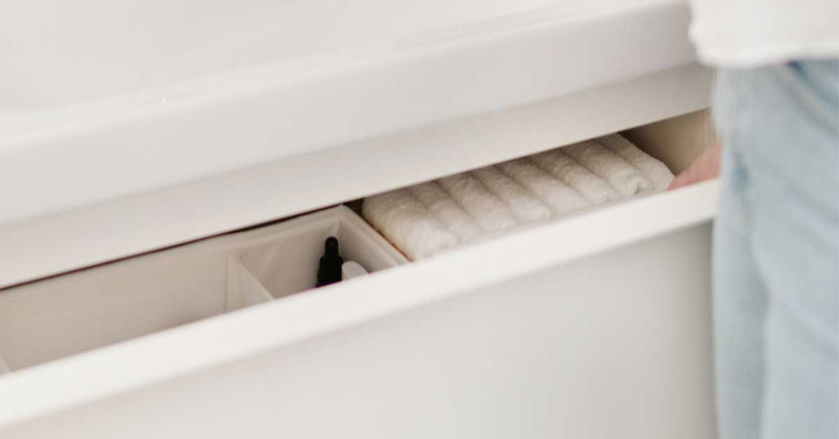 Person standing near open white bathroom drawer with organized items inside.