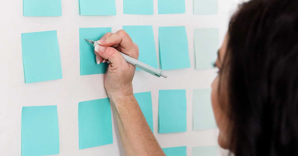 Woman having a planning session with blue sticky notes on wall.