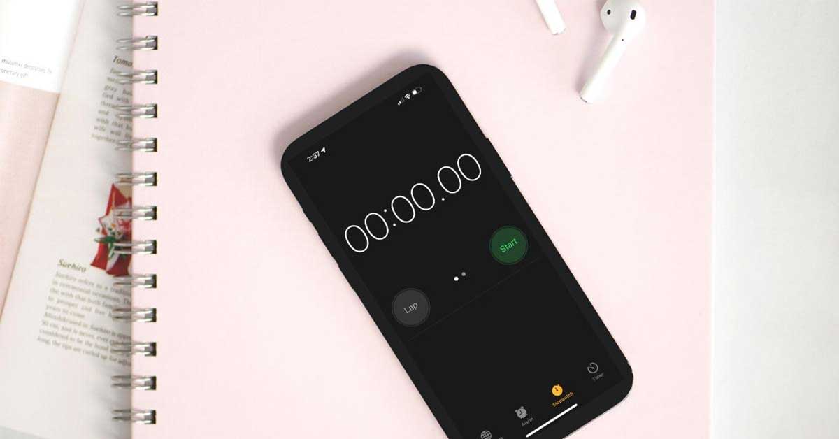 Phone showing stopwatch screen lying on pink planner and open magazine.