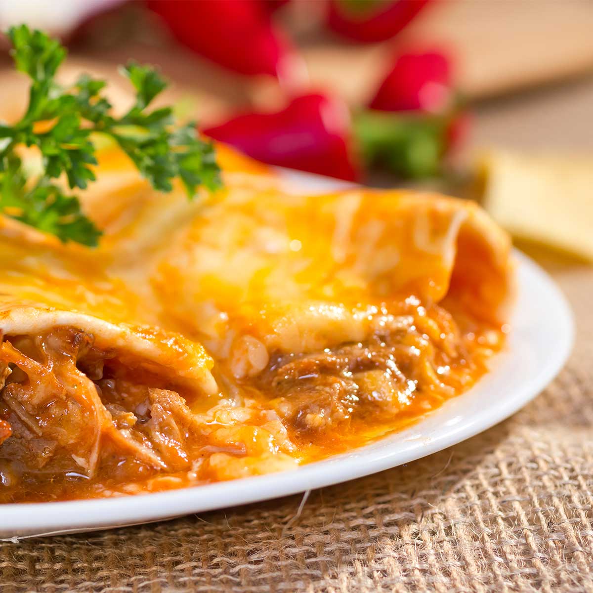 Beef enchiladas on white plate sitting on burlap placemat.