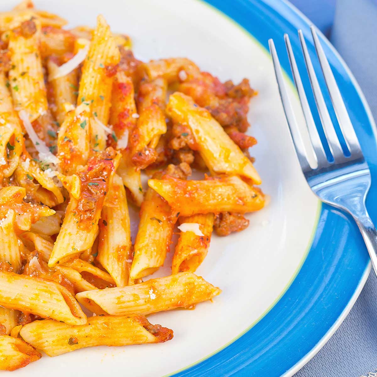 Beef penne and fork on blue and white plate.