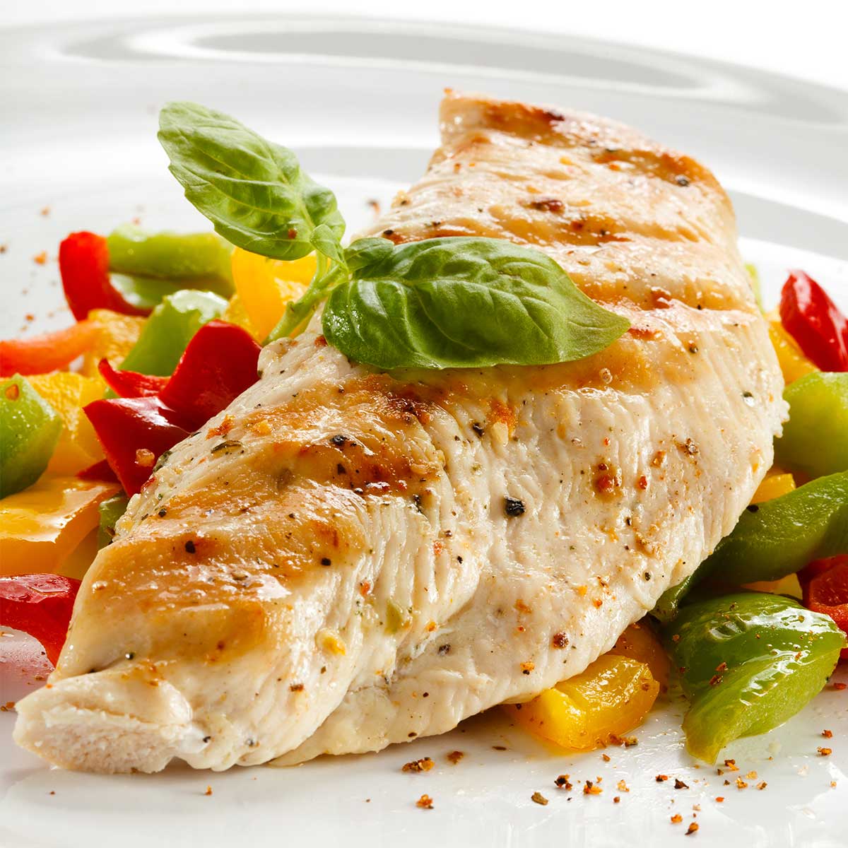 Close view of grilled chicken and peppers on white plate.