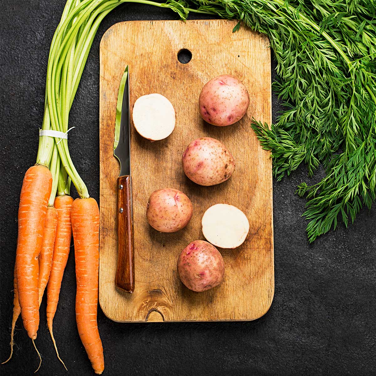 Carrots and potatoes on cutting board on dark countertop.