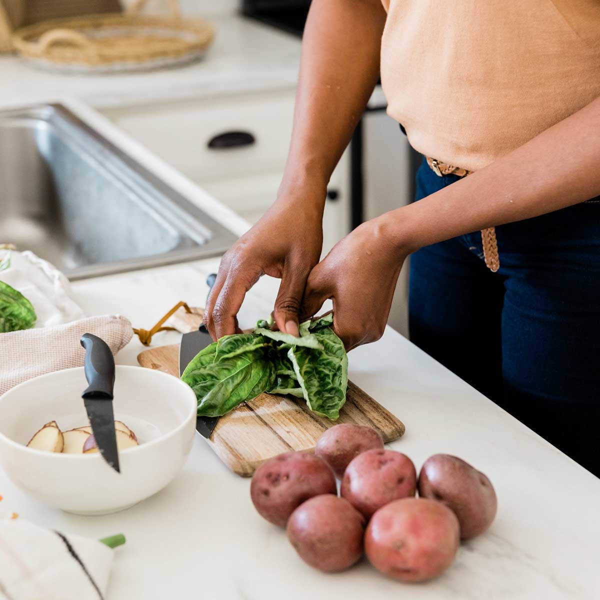 Woman preparing fresh ingredients for a meal in kitchen with white countertop.