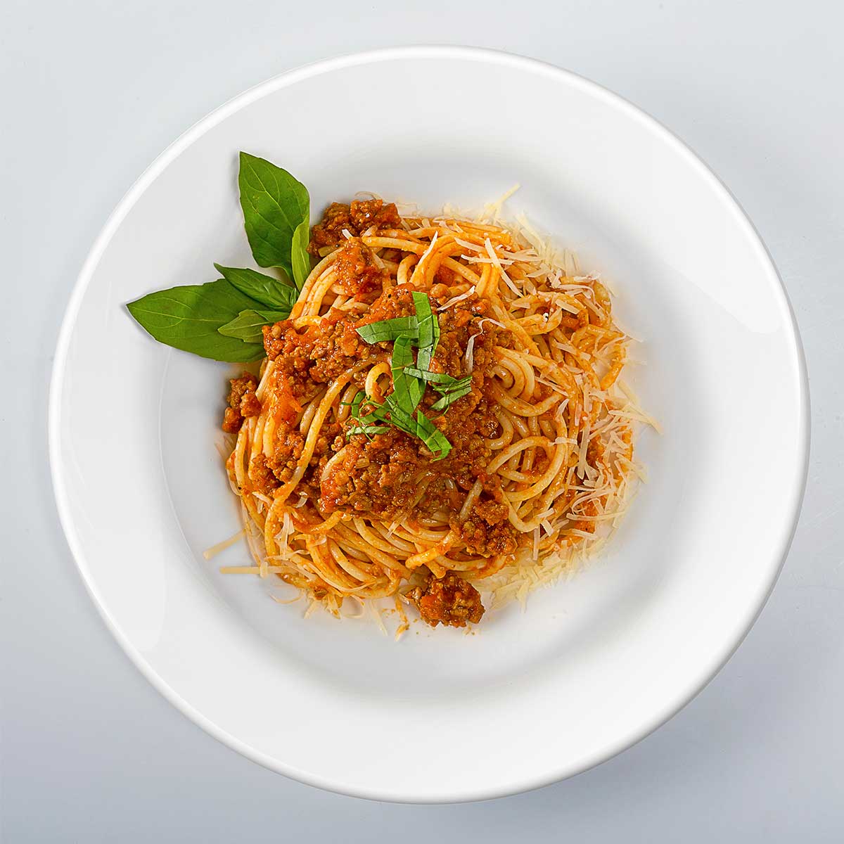 Spaghetti with sausage in white bowl sitting on white table.