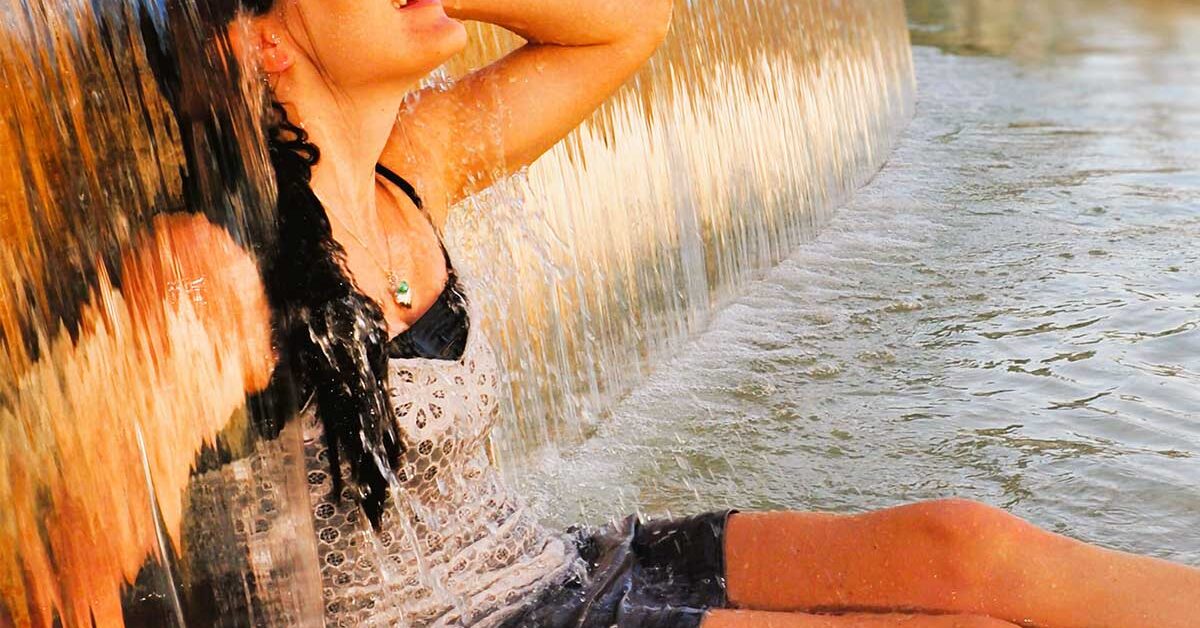 Woman sitting under fountain waterfall on a sunny hot summer day.