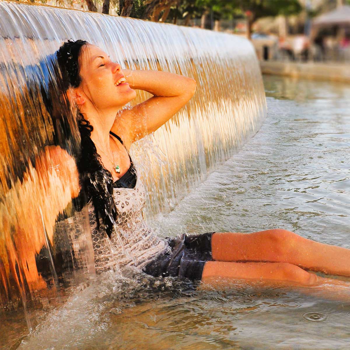 Woman sitting under fountain waterfall on a sunny hot summer day.