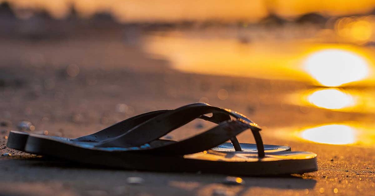 Flip-flops on deserted beach at sunset symbolizing the end of summer.