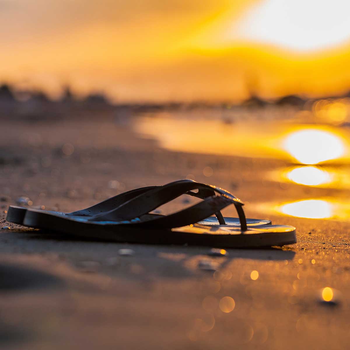 Flip-flops on deserted beach at sunset symbolizing the end of summer.