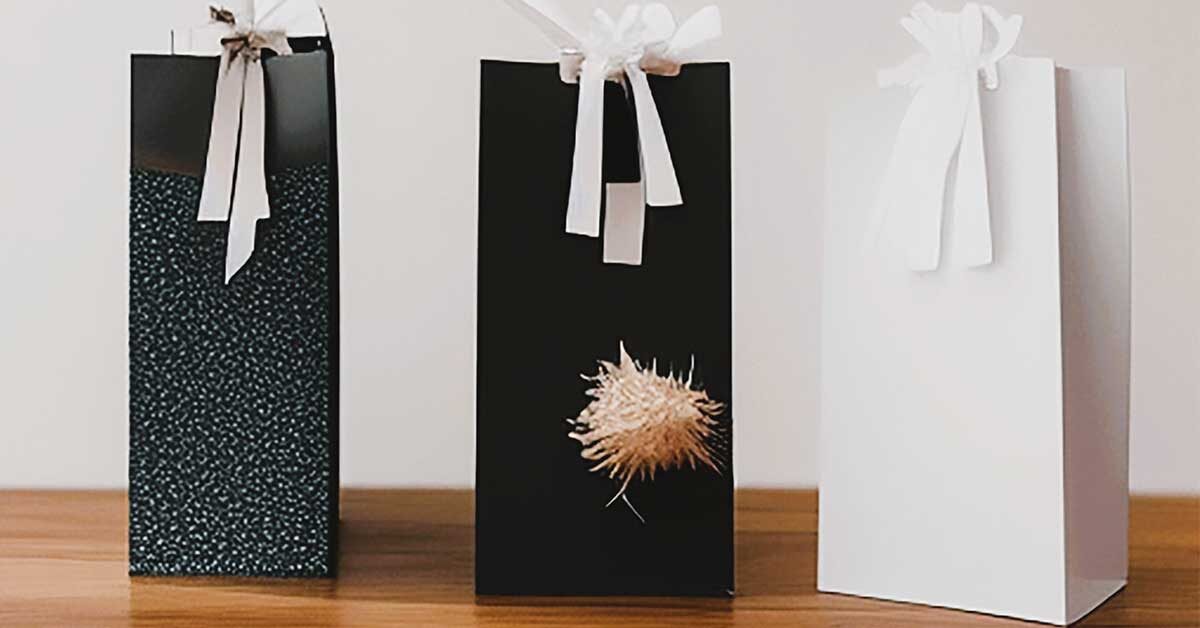 Three tall gift bags on wood table against white wall.