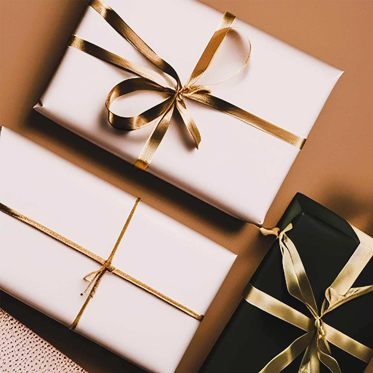 Black and white wrapped presents with gold ribbon on brown background.