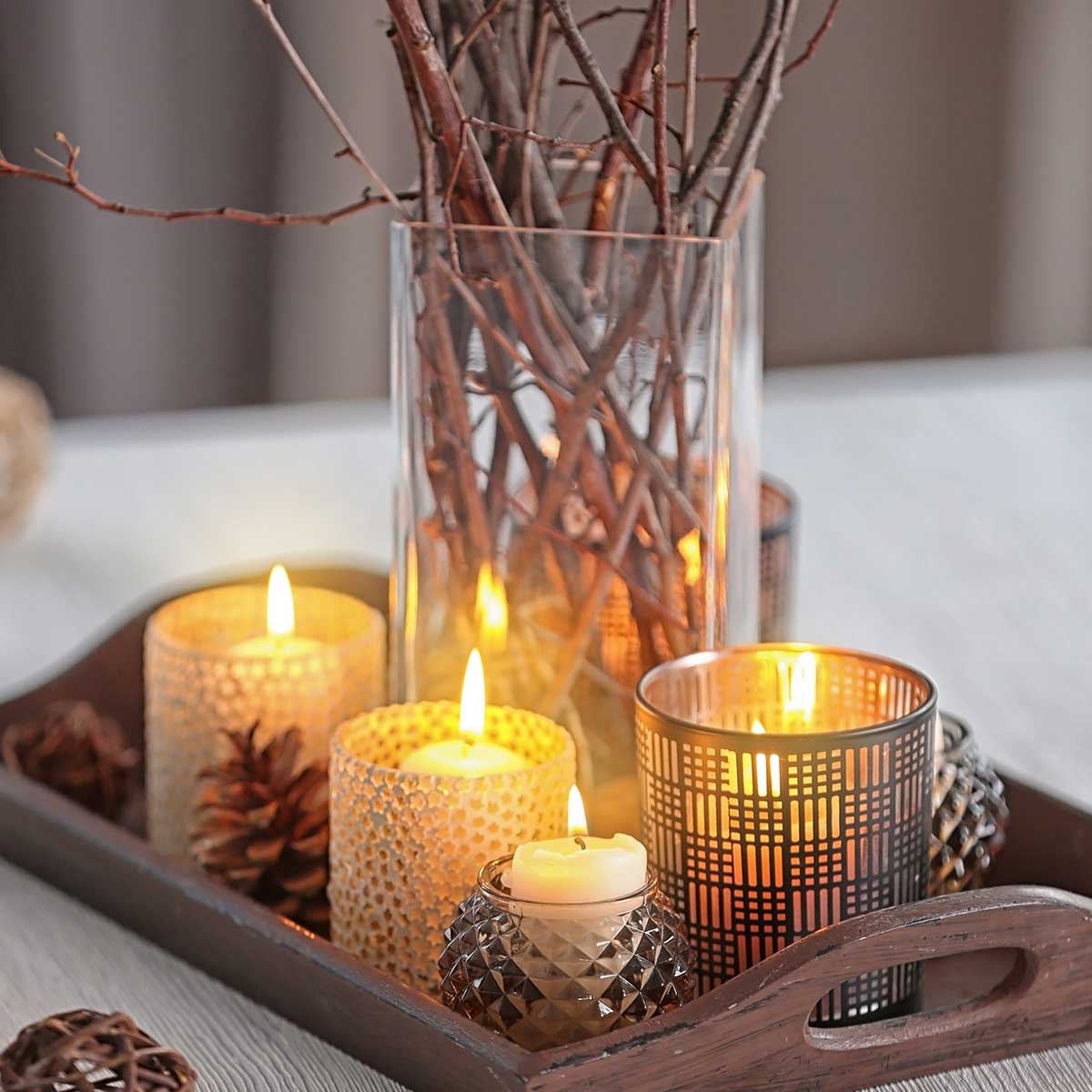 Candles and glass vase with bare branches on a wood tray.