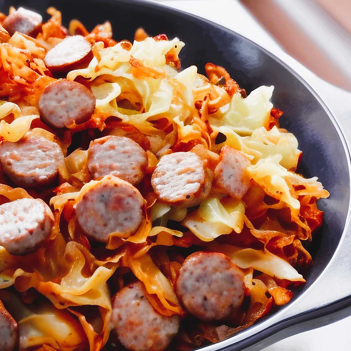 Fried cabbage and sausage in cast iron pan.