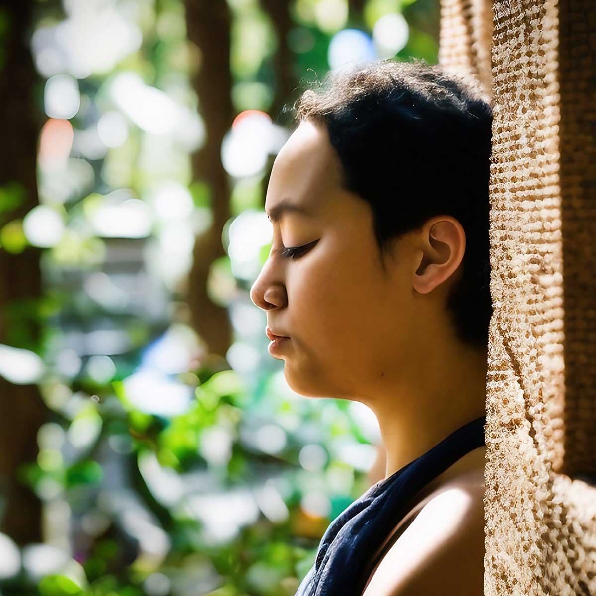 Profile view of woman pausing to be mindful during the day with bokeh-style greenery background.