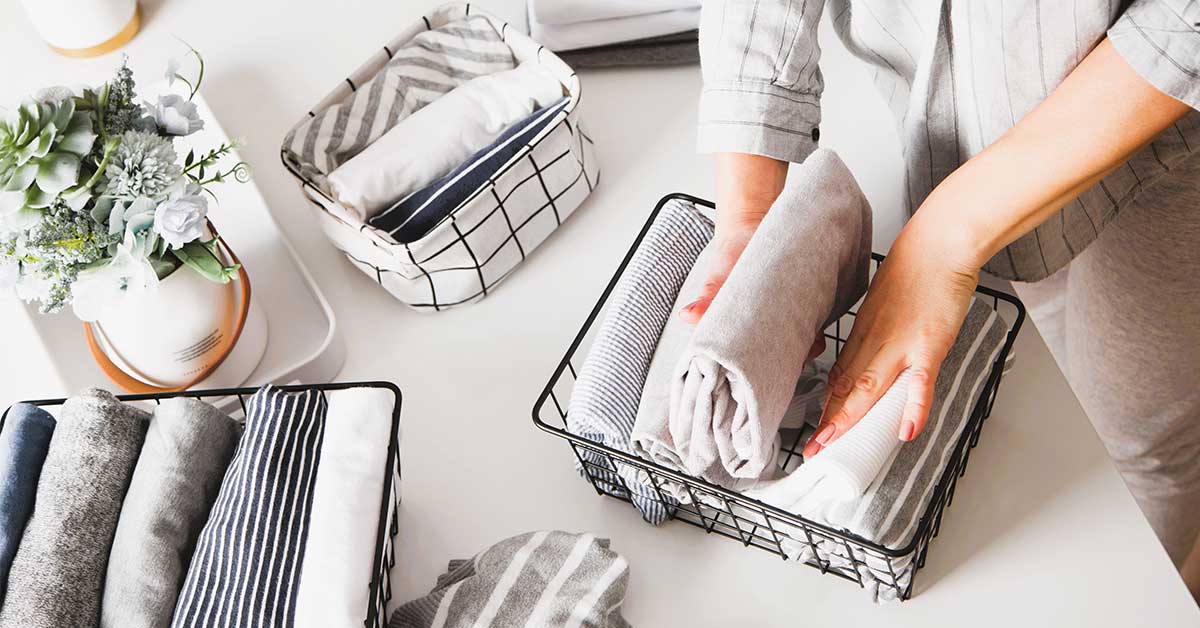 Woman folding clothes into inexpensive baskets for organizing a closet.