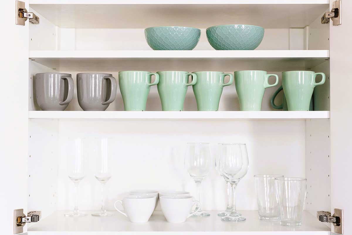 Organized white kitchen cabinet with glasses, mugs and bowls.