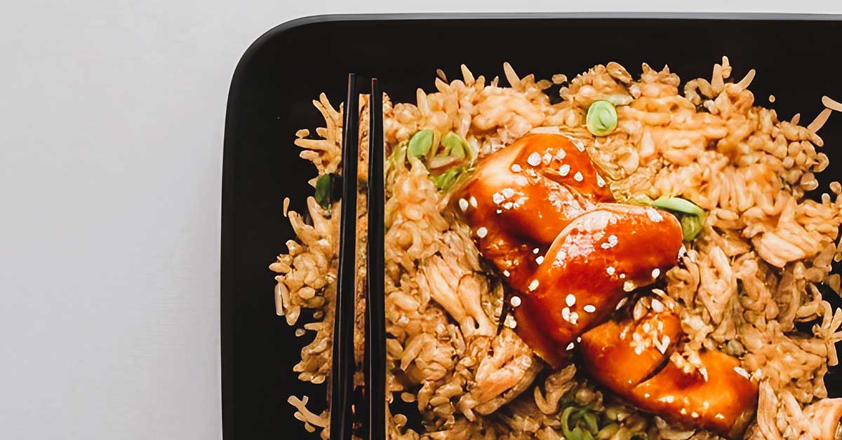 Teriyaki chicken and fried rice on black dish with chopsticks on gray countertop.