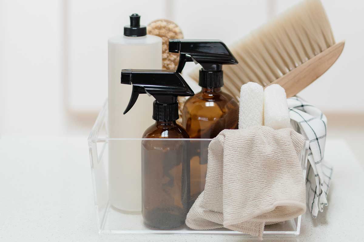 Cleaning supplies organized in a clear bin on a white countertop.