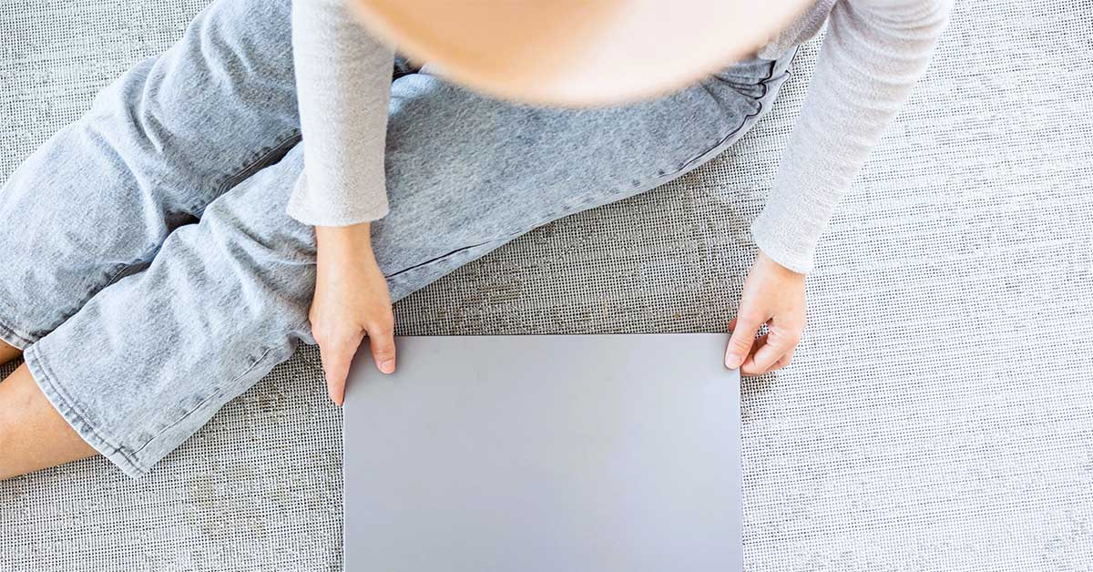 Top view of woman sitting on floor and preparing to open her laptop computer.