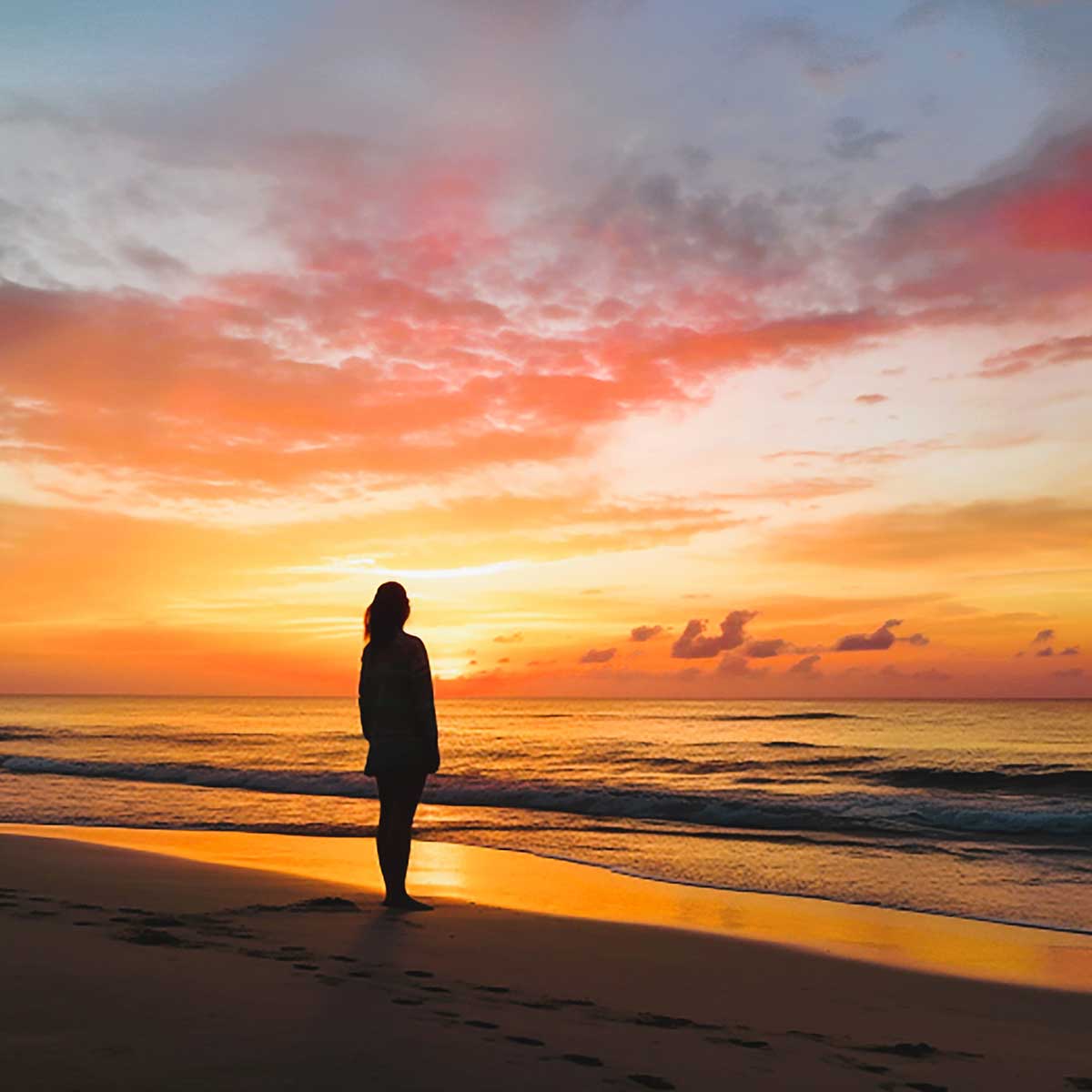 Woman standing on a beach watching a summer sunrise.