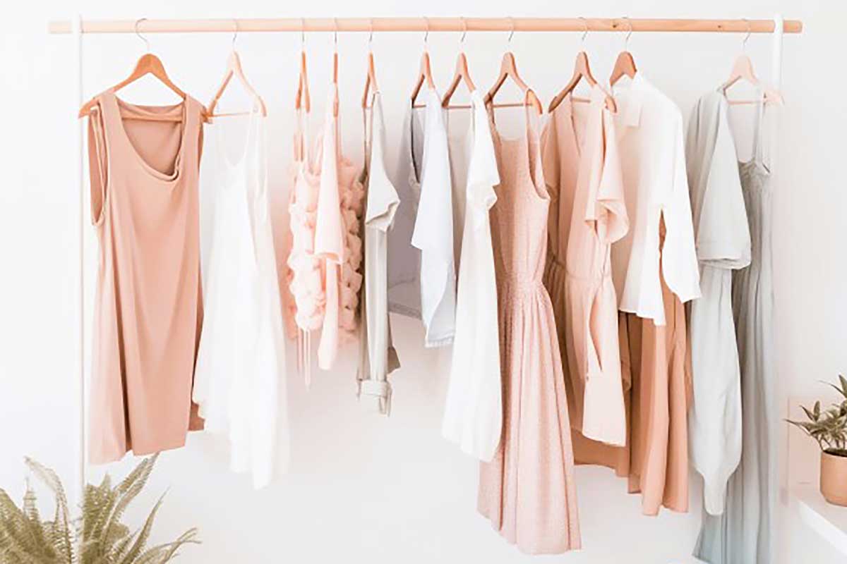 Clothing rack with an assortment of simple summer clothing in a white room.