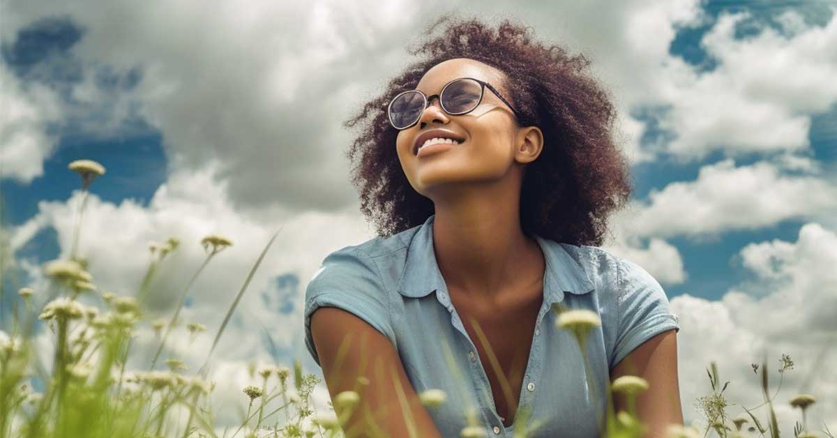 Smiling black woman focusing on today while sitting in meadow on sunny and cloudy day.