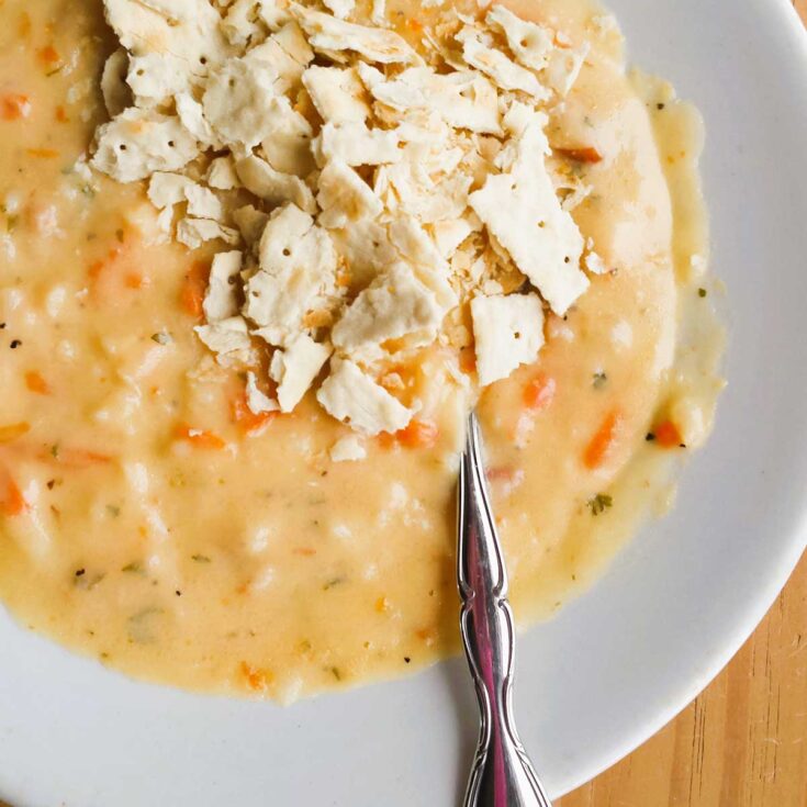 Canadian cheese soup and saltine crackers in white bowl with spoon on wood table.
