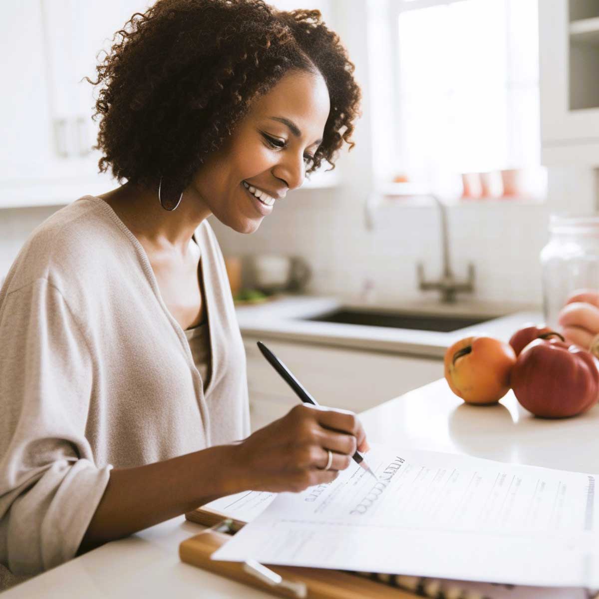 Black woman sitting in a kitchen to do monthly meal planning.